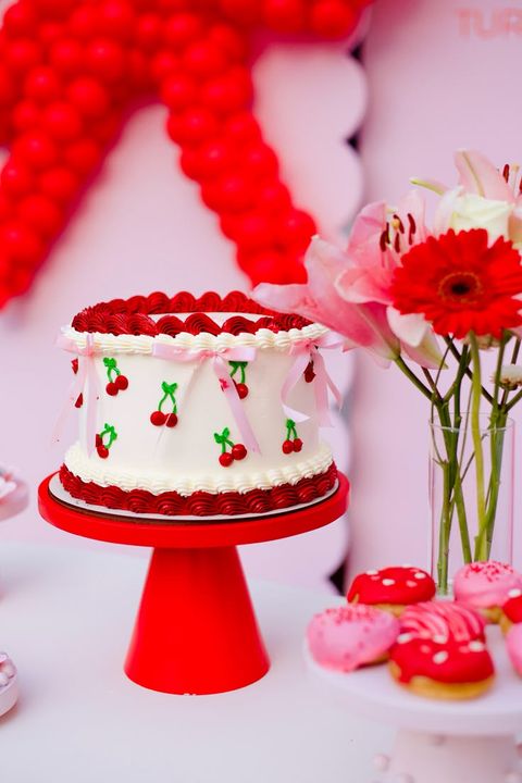Bolo de festa branco com cerejas desenhadas, laços rosa e suporte vermelho – Auris Doceria