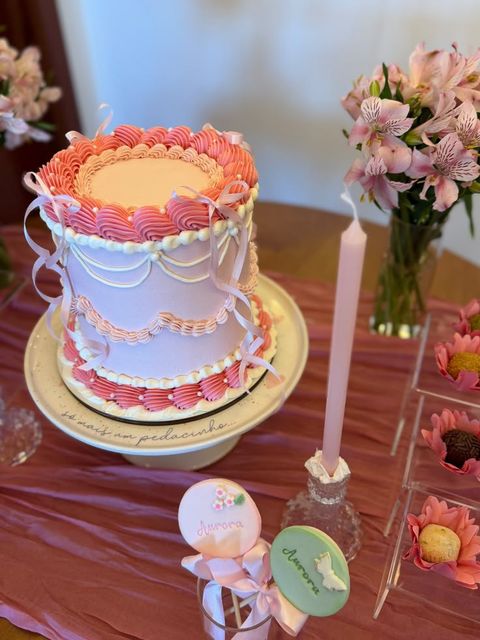 Bolo de festa rosa vintage com laços, biscoitos personalizados e flores na mesa – Auris Doceria