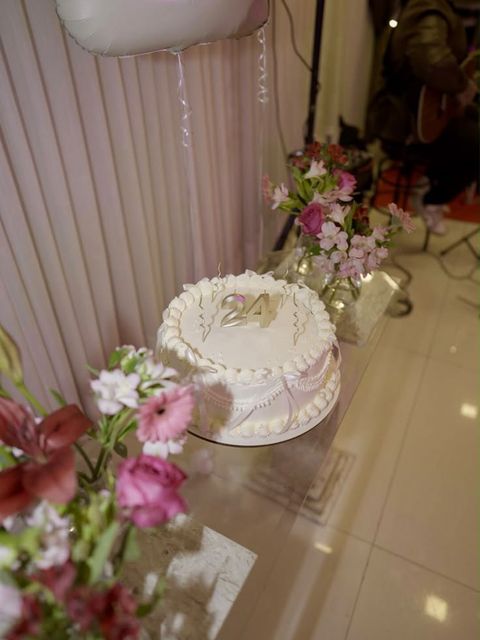 Bolo branco com topo dourado “24” em mesa de vidro com flores e balão – Auris Doceria